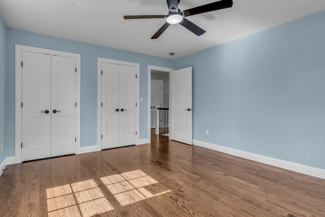 unfurnished bedroom with hardwood / wood-style flooring, ceiling fan, and multiple closets