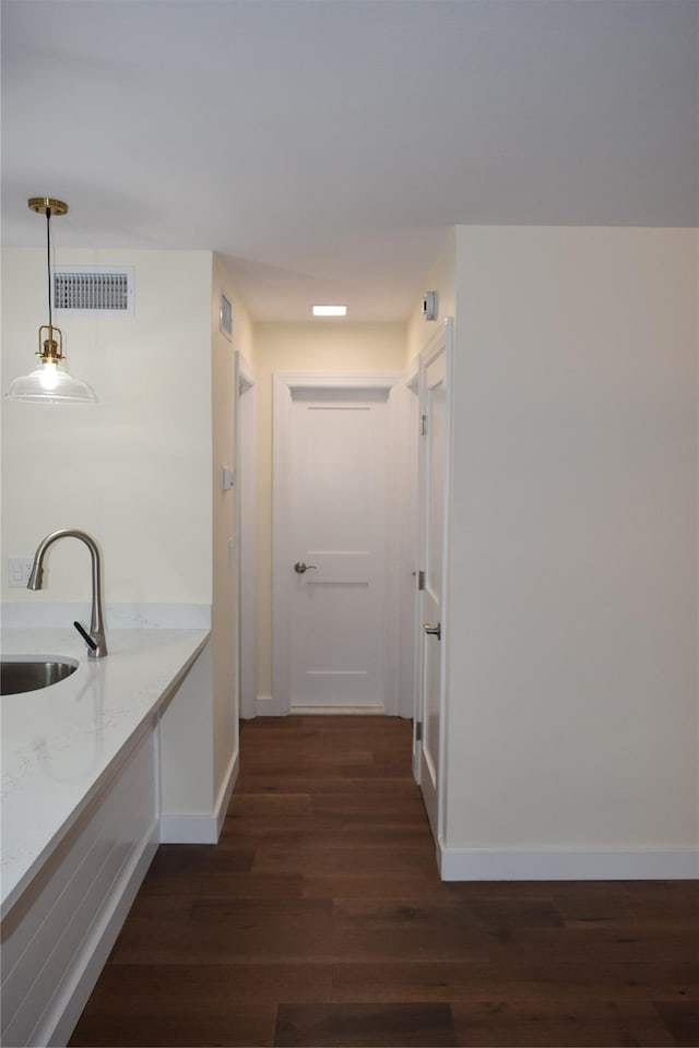 corridor featuring dark wood finished floors, a sink, visible vents, and baseboards