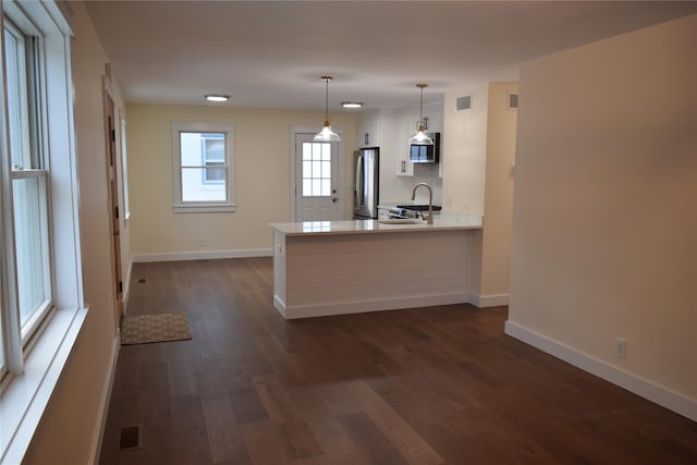 kitchen with stainless steel appliances, dark wood-type flooring, a peninsula, a sink, and visible vents