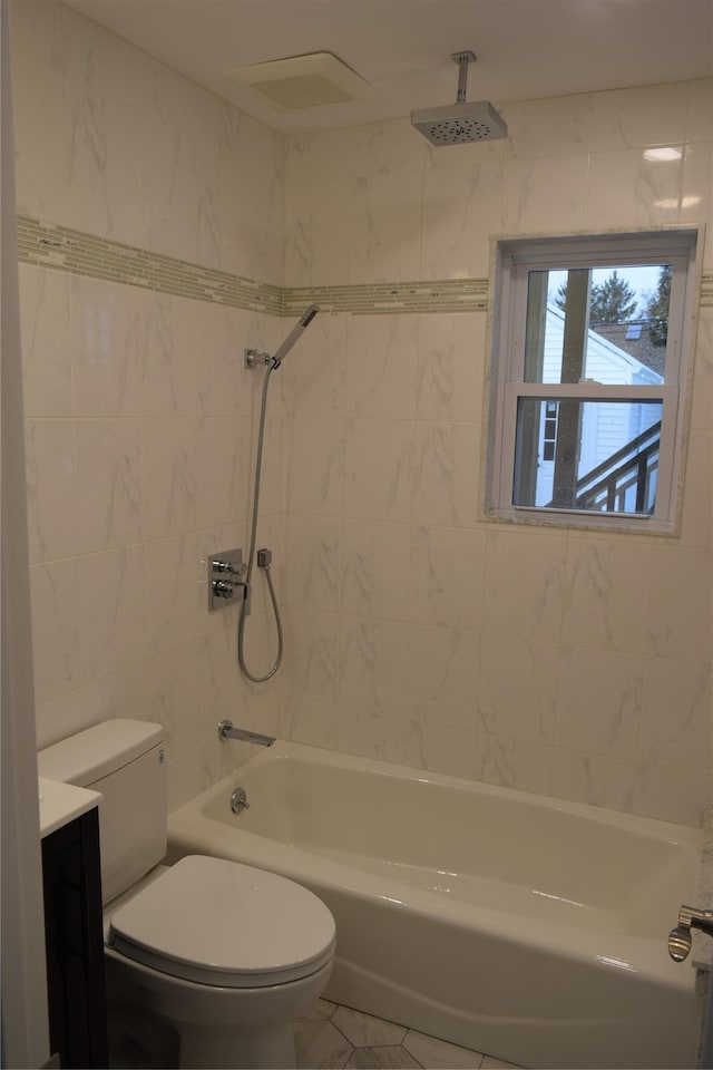 bathroom featuring tile walls, vanity, toilet, and a combined bath / shower with rainfall shower