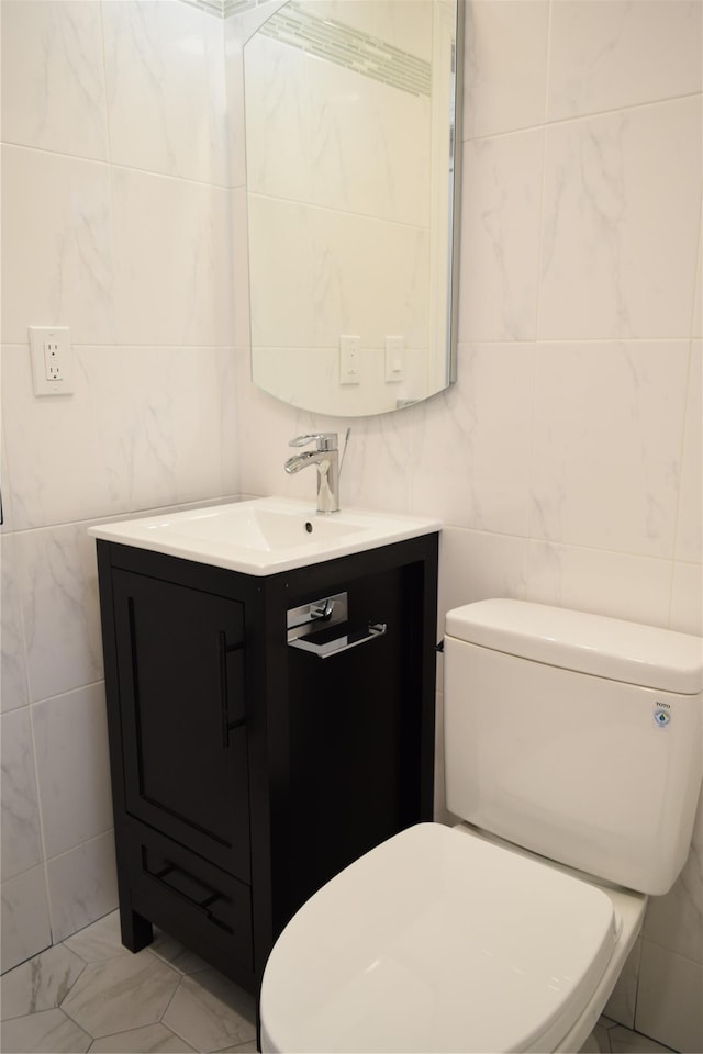 half bathroom with toilet, marble finish floor, tile walls, and vanity