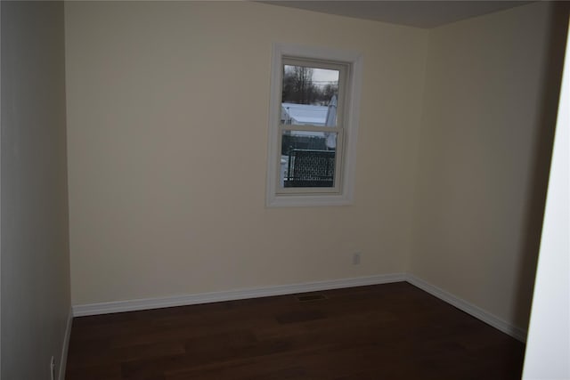 spare room featuring dark wood-style flooring, visible vents, and baseboards