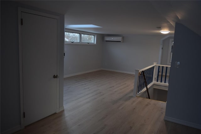 below grade area with an AC wall unit, wood finished floors, and baseboards