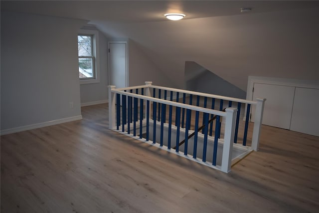 corridor with lofted ceiling, wood finished floors, an upstairs landing, and baseboards