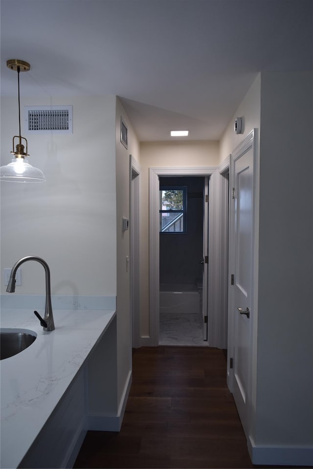 hall with dark wood-style floors, baseboards, visible vents, and a sink