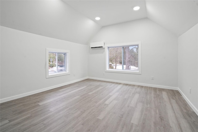 additional living space featuring plenty of natural light, vaulted ceiling, light hardwood / wood-style flooring, and an AC wall unit