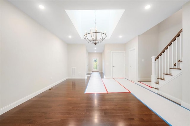 foyer with a raised ceiling, an inviting chandelier, and dark wood-type flooring