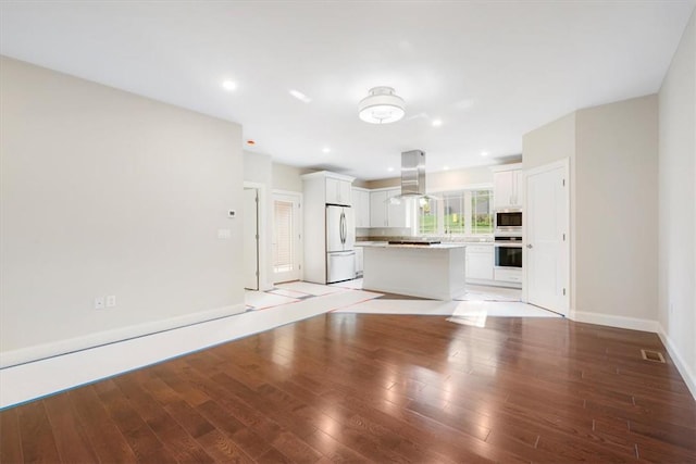 kitchen with a center island, island exhaust hood, oven, white fridge, and white cabinets