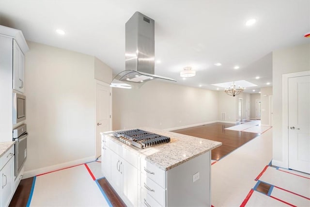 kitchen with appliances with stainless steel finishes, a center island, island range hood, and white cabinetry