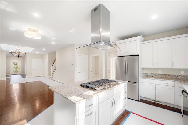 kitchen featuring island exhaust hood, appliances with stainless steel finishes, light stone counters, white cabinets, and a kitchen island