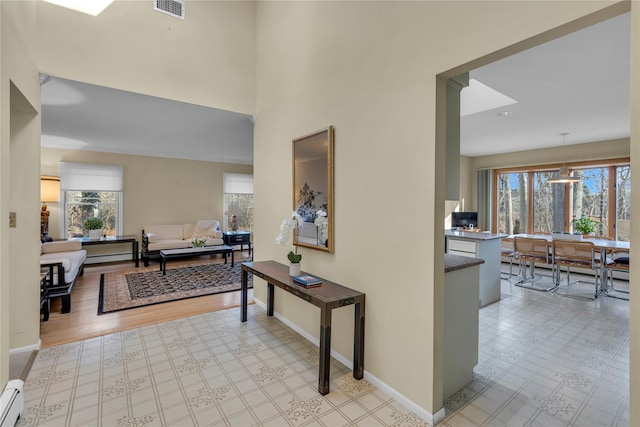 hallway featuring light wood-type flooring, a baseboard radiator, an inviting chandelier, and a healthy amount of sunlight