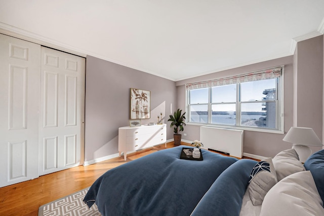 bedroom with wood-type flooring, a water view, a closet, and crown molding