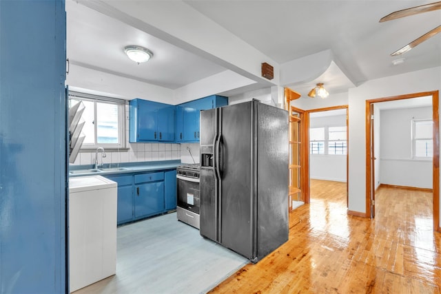 kitchen with backsplash, black refrigerator with ice dispenser, sink, blue cabinetry, and gas stove