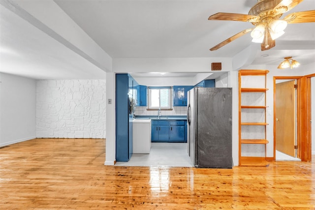 kitchen featuring black refrigerator, light wood-type flooring, tasteful backsplash, blue cabinets, and sink