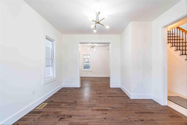 unfurnished room with a notable chandelier and dark hardwood / wood-style flooring