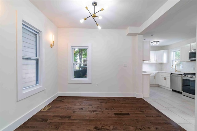 unfurnished dining area with sink, a chandelier, a wealth of natural light, and dark hardwood / wood-style floors