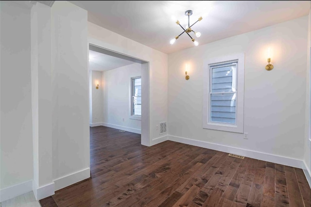 spare room featuring an inviting chandelier and dark hardwood / wood-style floors