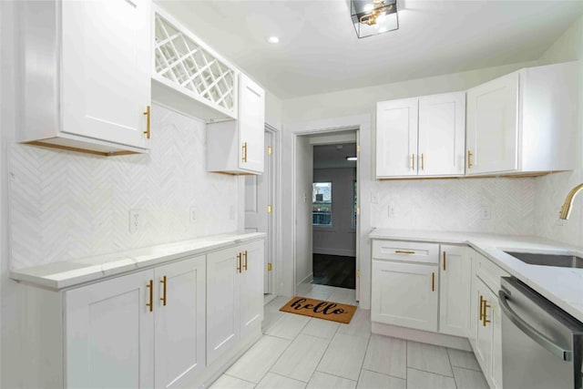 kitchen featuring light stone counters, white cabinets, dishwasher, and sink