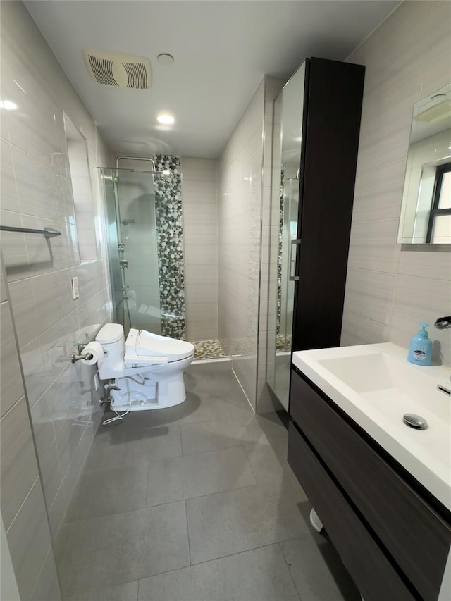 bathroom featuring tile patterned floors, vanity, tiled shower, tile walls, and toilet