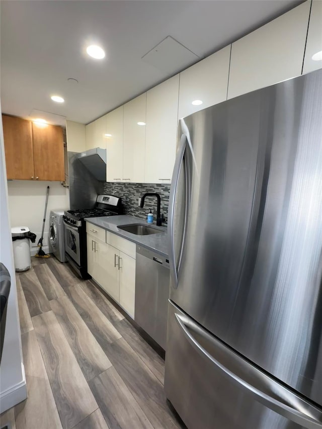 kitchen with sink, stainless steel appliances, washer / dryer, white cabinets, and hardwood / wood-style flooring