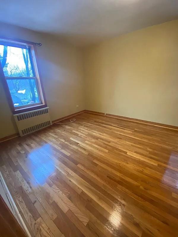 unfurnished room with hardwood / wood-style flooring and radiator heating unit