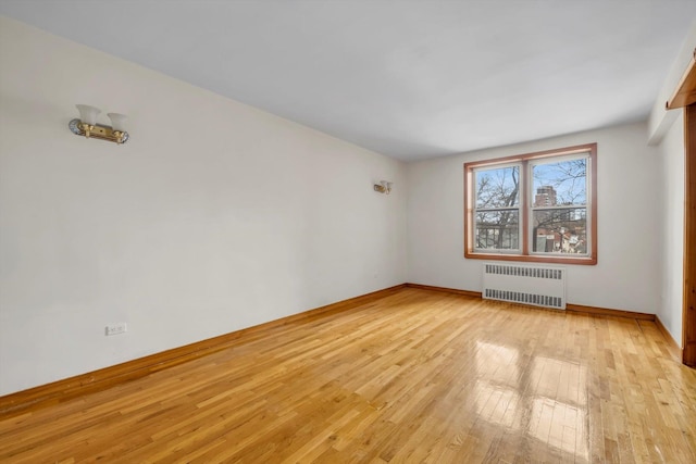 empty room featuring light wood-type flooring, baseboards, and radiator heating unit