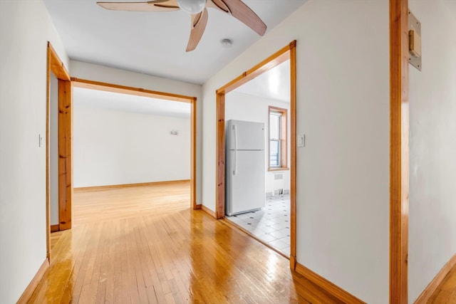 hallway with radiator heating unit, baseboards, and light wood finished floors