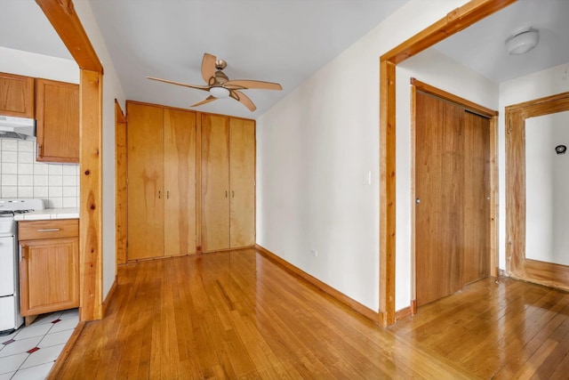 interior space featuring under cabinet range hood, light wood-style floors, light countertops, range, and decorative backsplash