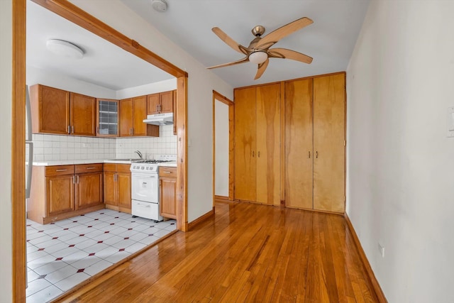 kitchen featuring tasteful backsplash, white range with gas cooktop, glass insert cabinets, light countertops, and under cabinet range hood