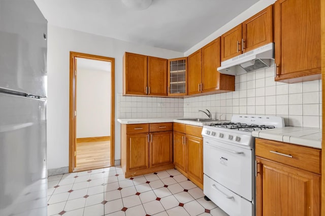 kitchen featuring under cabinet range hood, light countertops, freestanding refrigerator, white gas range, and glass insert cabinets