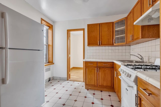 kitchen featuring under cabinet range hood, white appliances, light countertops, radiator, and glass insert cabinets