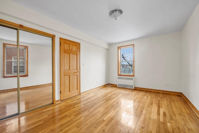 unfurnished bedroom featuring baseboards, a closet, light wood-type flooring, and radiator