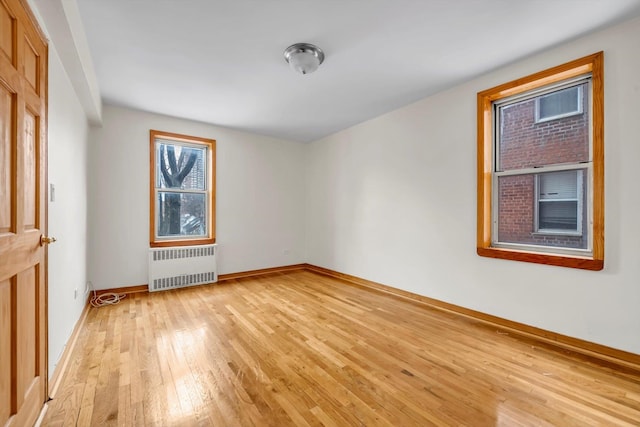 empty room featuring radiator heating unit, baseboards, and light wood-style flooring