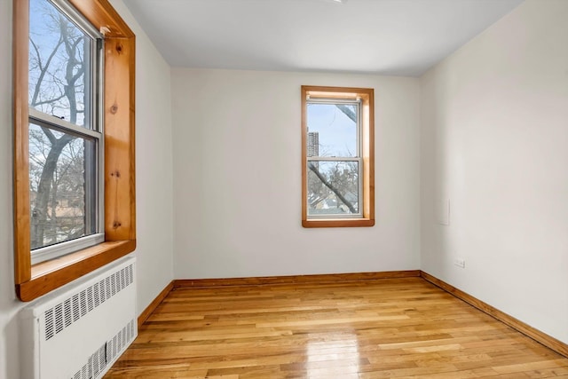 empty room featuring light wood finished floors, radiator heating unit, and baseboards