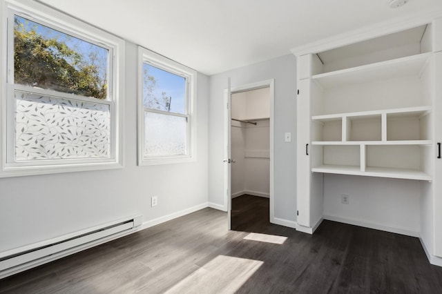 unfurnished bedroom featuring baseboard heating, a walk in closet, a closet, and dark hardwood / wood-style flooring