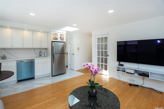 kitchen featuring a skylight, white cabinetry, stainless steel appliances, tasteful backsplash, and crown molding