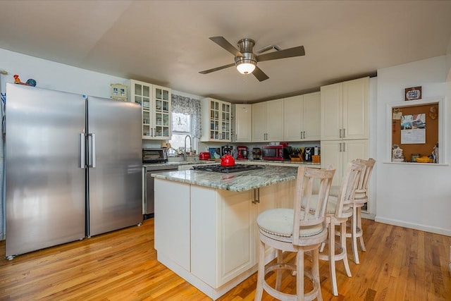 kitchen with appliances with stainless steel finishes, light wood-type flooring, light stone counters, ceiling fan, and a kitchen island