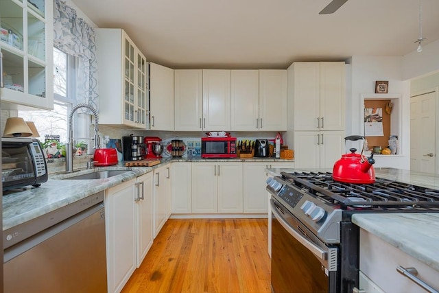 kitchen with white dishwasher, sink, gas stove, light stone counters, and white cabinetry