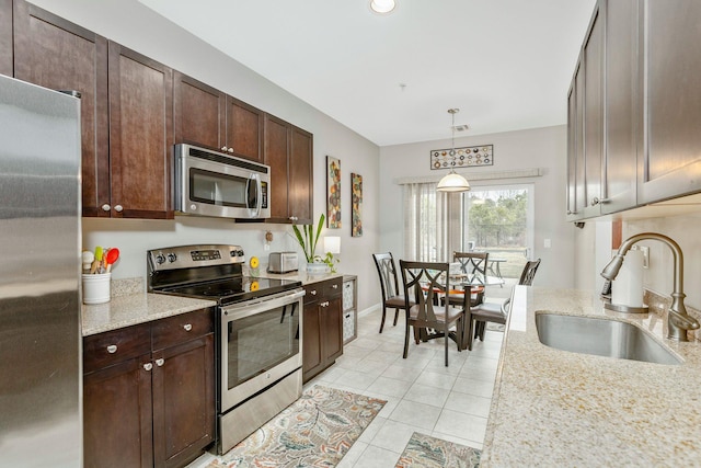 kitchen with stainless steel appliances, dark brown cabinets, pendant lighting, light stone counters, and sink