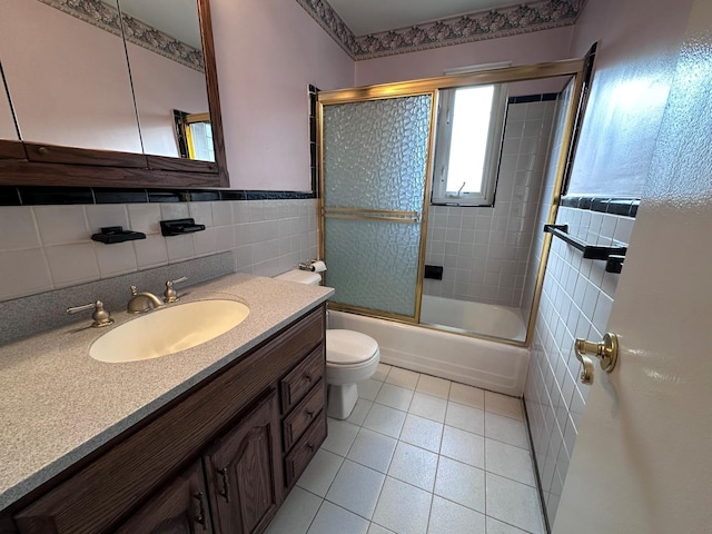 full bathroom featuring tile patterned floors, bath / shower combo with glass door, toilet, vanity, and tile walls