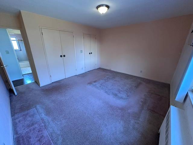 unfurnished bedroom featuring dark carpet and two closets