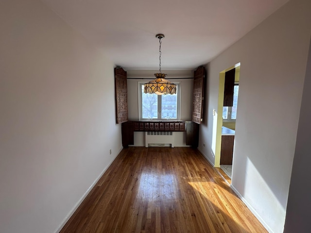 unfurnished dining area featuring radiator heating unit and hardwood / wood-style flooring