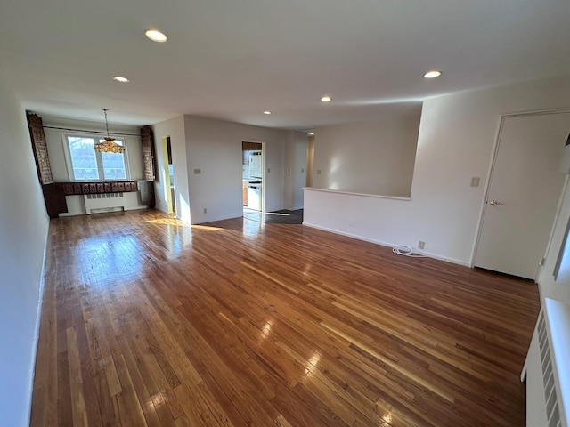 unfurnished living room featuring a notable chandelier, dark hardwood / wood-style floors, and radiator heating unit