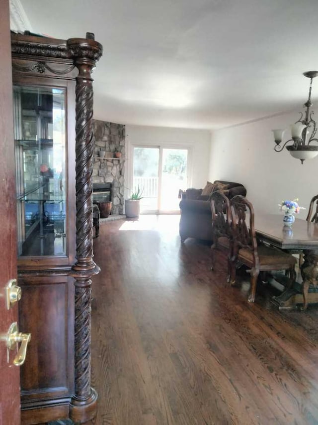 dining space with a stone fireplace, dark wood-type flooring, and an inviting chandelier