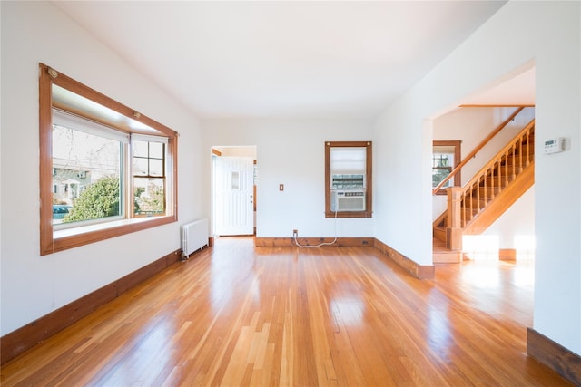 unfurnished living room featuring radiator heating unit, cooling unit, and light wood-type flooring