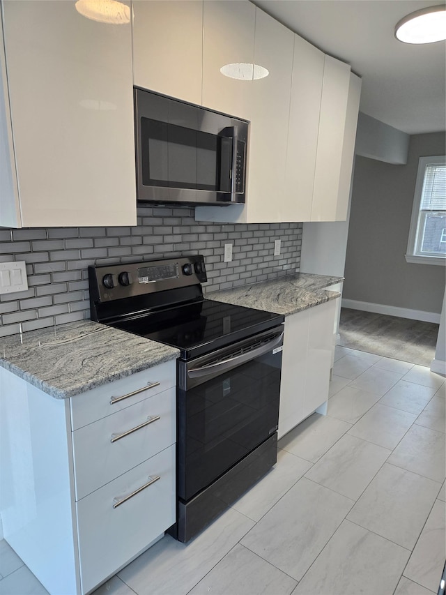 kitchen with backsplash, black electric range, light stone countertops, light tile patterned flooring, and white cabinetry