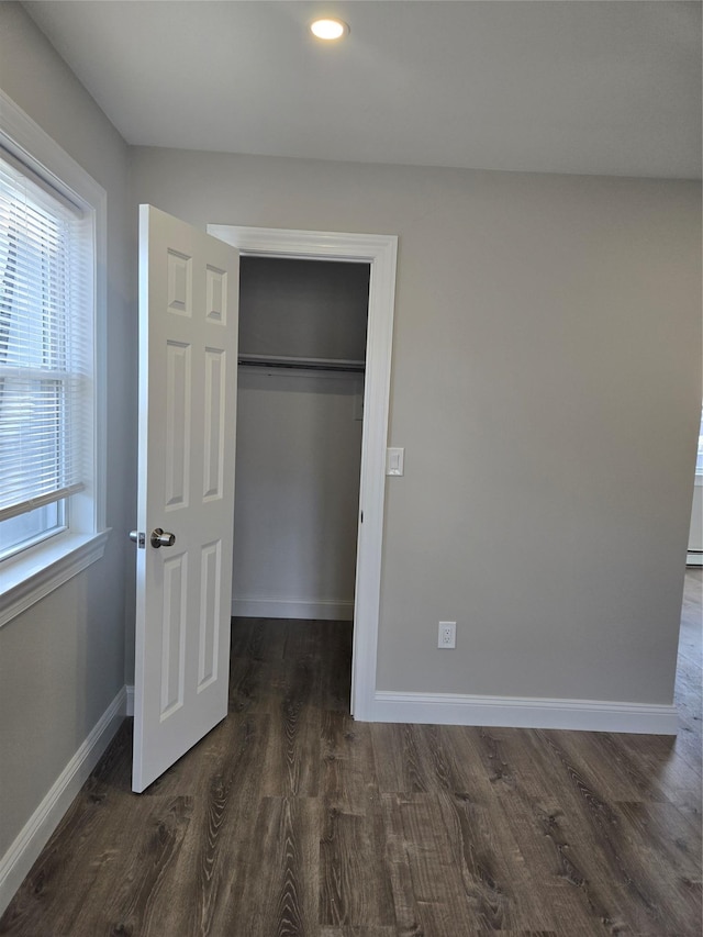 unfurnished bedroom featuring multiple windows, a closet, and dark wood-type flooring