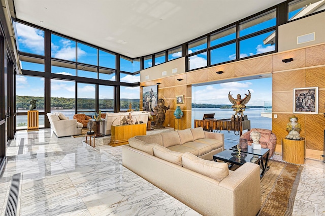 living room with a high ceiling, a water view, and wood walls