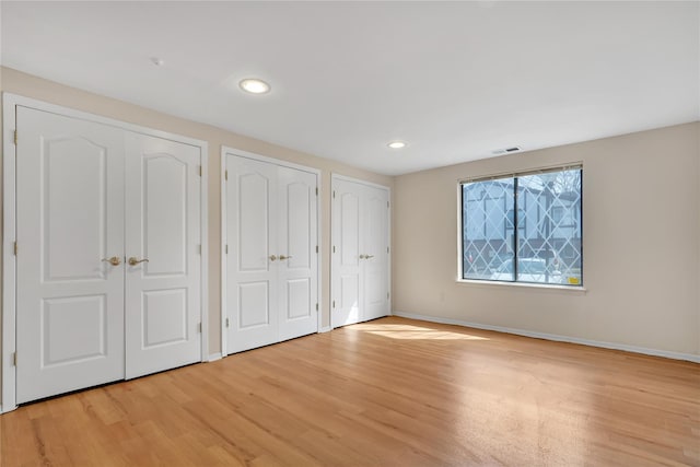 unfurnished bedroom featuring two closets and light wood-type flooring