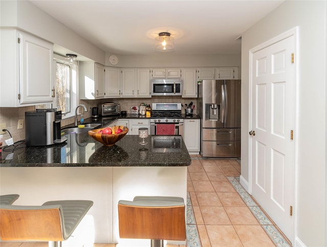 kitchen featuring dark stone counters, white cabinets, sink, kitchen peninsula, and stainless steel appliances